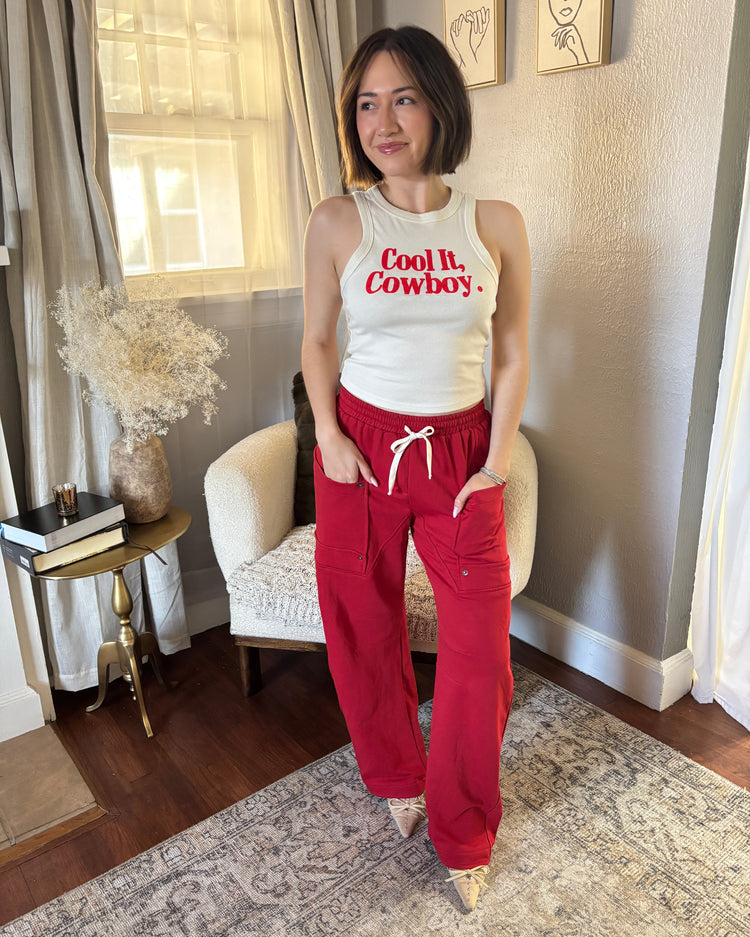 wearing a white tank top with red text and red pants in a room.